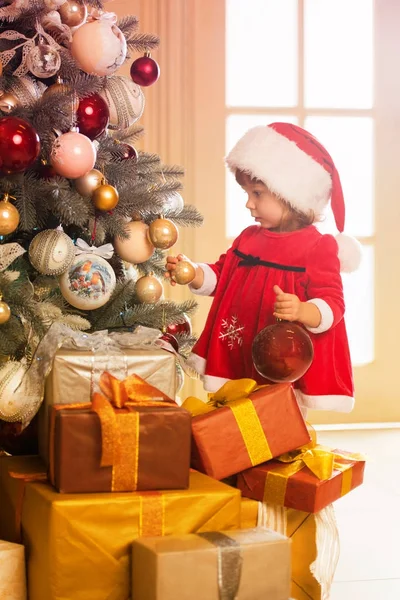 Feliz Navidad y Felices Fiestas. Linda niña está decorando el árbol de Navidad en el interior . —  Fotos de Stock