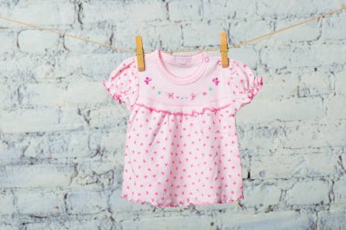 Beyaz duvara karşı bir ip üzerinde bir bebek elbise kurur.