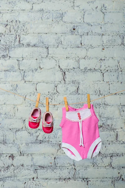 Childrens pink body, bib and red shoes, dry on a rope against a white brick wall. — Stock Photo, Image