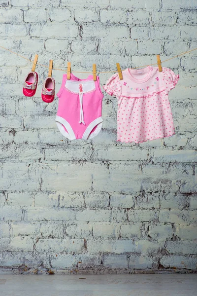 Niños de color rosa bodic, vestido y zapatos rojos para la niña, seco en una cuerda contra una pared de ladrillo blanco . — Foto de Stock