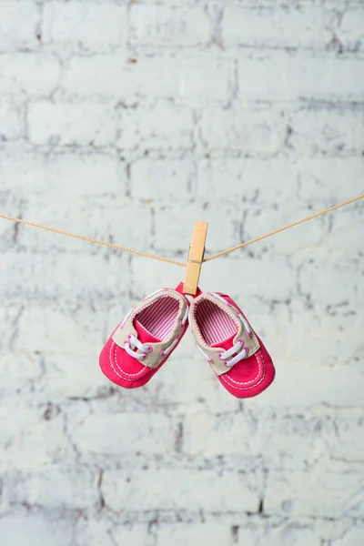 Baby rode schoenen aan een touw tegen een witte muur. — Stockfoto