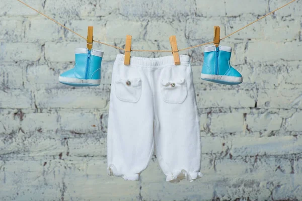 Botas para niños y pantimedias secas en una cuerda contra una pared de ladrillo blanco . —  Fotos de Stock