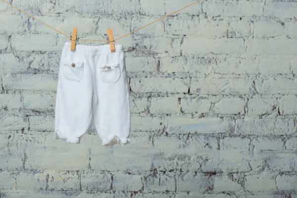 Meia-calça de bebê seca em uma corda contra uma parede de tijolo branco . — Fotografia de Stock