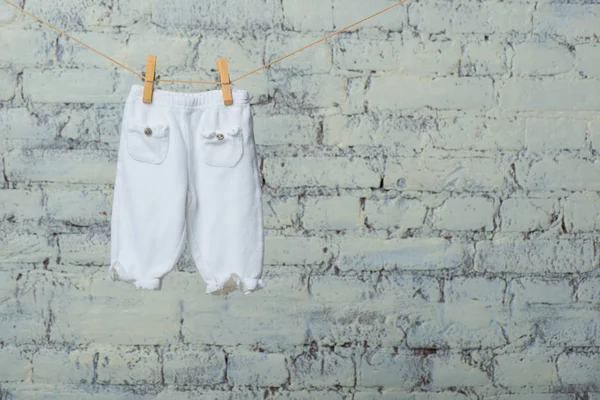 Baby pantyhose dry on a rope against a white brick wall. — Stock Photo, Image