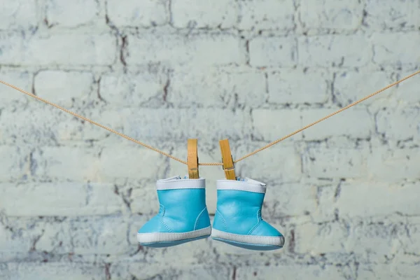 Las botas infantiles secan por la cuerda contra la pared blanca de ladrillo . — Foto de Stock