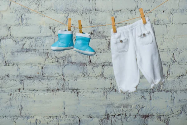 Botas para niños y pantimedias secas en una cuerda contra una pared de ladrillo blanco . — Foto de Stock