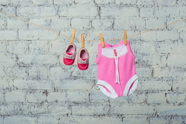 Childrens rosa kropp, Haklapp och röda skor, torka på ett rep mot en vit tegelvägg. — Stockfoto