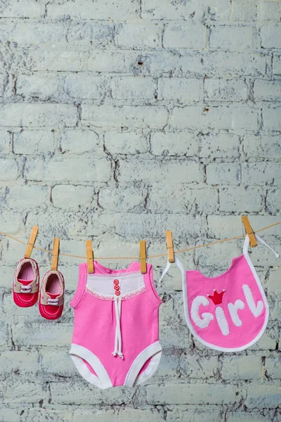 Childrens pink body, bib and red shoes, dry on a rope against a white brick wall. — Stock Photo, Image