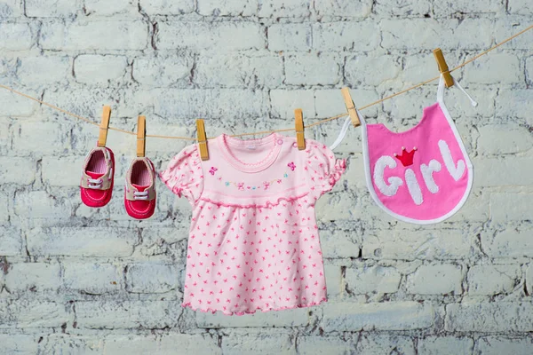 Babero de los niños, vestido y zapatos rojos para la niña, seco en una cuerda en una pared de ladrillo blanco . — Foto de Stock