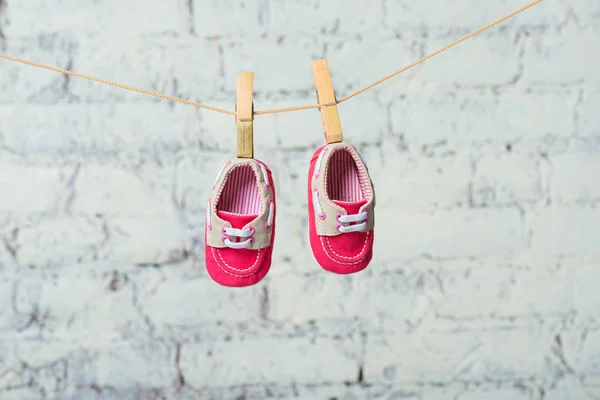Bebé zapatos rojos en una cuerda contra una pared de ladrillo blanco . — Foto de Stock