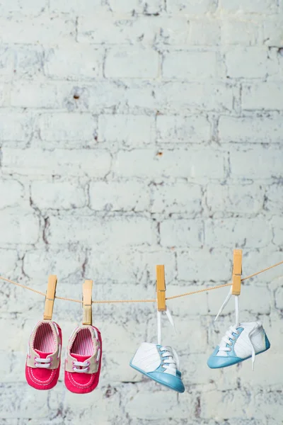 Baby blå och röda skor på ett rep mot en vit tegelvägg. — Stockfoto