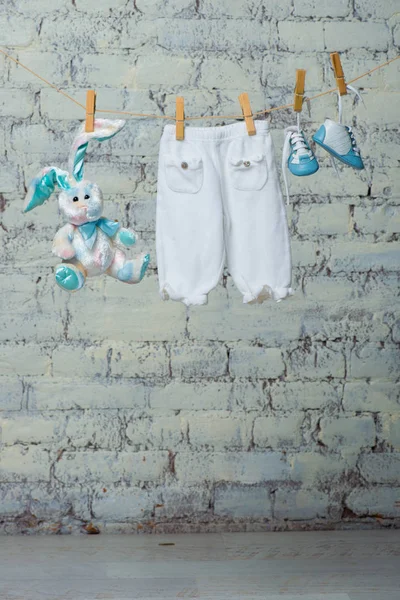 Детский белый бодик, сапоги, трусики и сухой игрушечный кролик на веревке у стены из белого кирпича . — стоковое фото