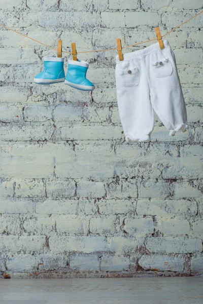 Stivali per bambini e collant asciutti su una corda contro un muro di mattoni bianchi . — Foto Stock