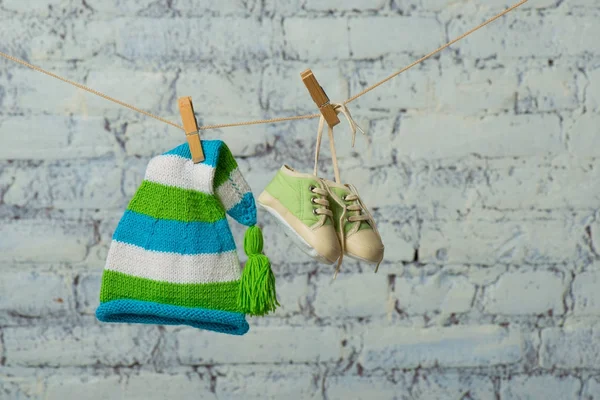 Babymütze und Turnschuhe trocknen auf einem Seil an einer weißen Ziegelwand. — Stockfoto