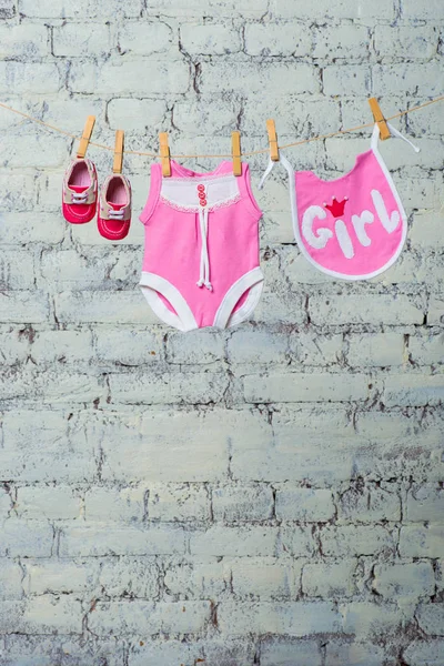 Childrens pink body, bib and red shoes, dry on a rope against a white brick wall. — Stock Photo, Image