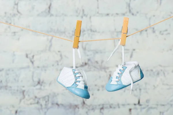 Sapatos azuis de bebê em uma corda contra uma parede de tijolo branco . — Fotografia de Stock