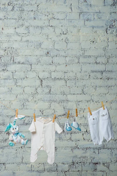 Bodik bianco da bambini, stivali, mutandine e un coniglio giocattolo si asciugano su una corda contro un muro di mattoni bianchi . — Foto Stock