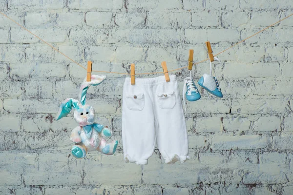 Bodik branco de crianças, botas, calcinha e um coelho de brinquedo secam em uma corda contra uma parede de tijolo branca . — Fotografia de Stock