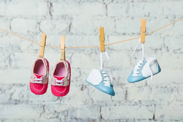 Baby blaue und rote Schuhe an einem Seil gegen eine weiße Ziegelwand. — Stockfoto