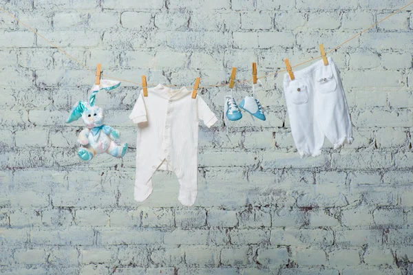 Childrens white bodik, boots, panties and a toy rabbit dry on a rope against a white brick wall. — Stock Photo, Image