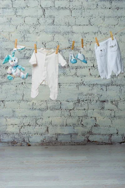 Niños cuerpo blanco, botas, bragas y un conejo de juguete seco en una cuerda contra una pared de ladrillo blanco . — Foto de Stock