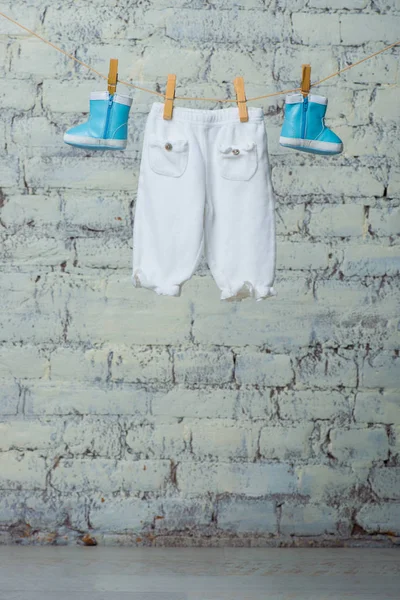 Bottes et collants pour enfants secs sur une corde contre un mur de briques blanches . — Photo