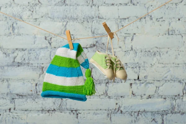 Gorra de bebé y zapatillas se secarán en una cuerda en una pared de ladrillo blanco . — Foto de Stock