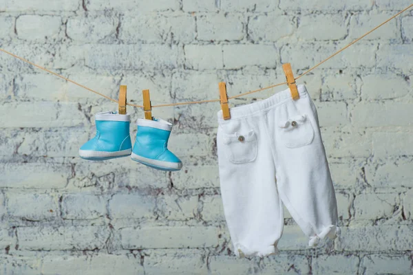 Botas de crianças e meia-calça seca em uma corda contra uma parede de tijolo branca . — Fotografia de Stock