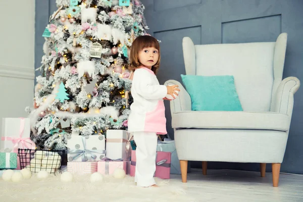 Petite fille souriante émotionnelle en pyjama avec cadeaux de Noël près de l'arbre du Nouvel An et cheminée décorée — Photo