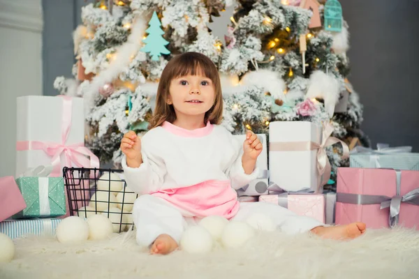 Emotional smiling little girl sitting in pajama with Christmas gifts near New Years tree and playing snowballs — Stock Photo, Image