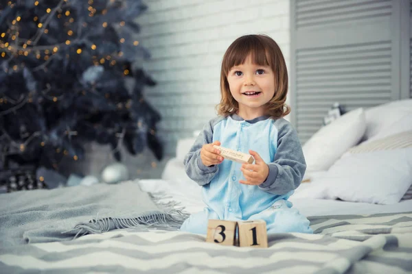 Маленька мила дівчинка 2 роки сидить біля ялинки і дивиться на календар. 31 грудня . — стокове фото