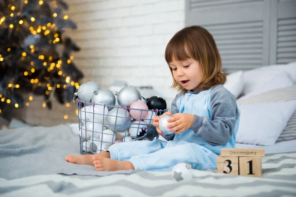 Small cute little girl is 2 years old sitting near Christmas tree and looking at the calendar. 31th of December. — Stock Photo, Image