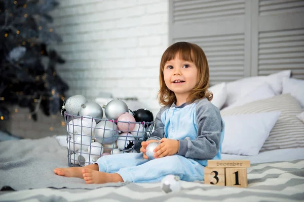 Mały uroczy dziewczynka jest 2 lat, siedzący w pobliżu choinki i patrząc na kalendarz. 31 grudnia. — Zdjęcie stockowe