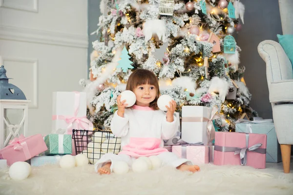 Emocional niña sonriente sentada en pijama con regalos de Navidad cerca del árbol de Año Nuevo y jugando bolas de nieve —  Fotos de Stock