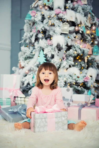 Niña alegre positiva sentada con regalo de Navidad cerca del árbol de Navidad. Feliz Año Nuevo —  Fotos de Stock