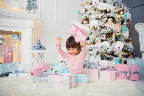 Positieve vrolijke babymeisje zit met de gift van Kerstmis in de buurt van de kerstboom. Gelukkig Nieuwjaar — Stockfoto