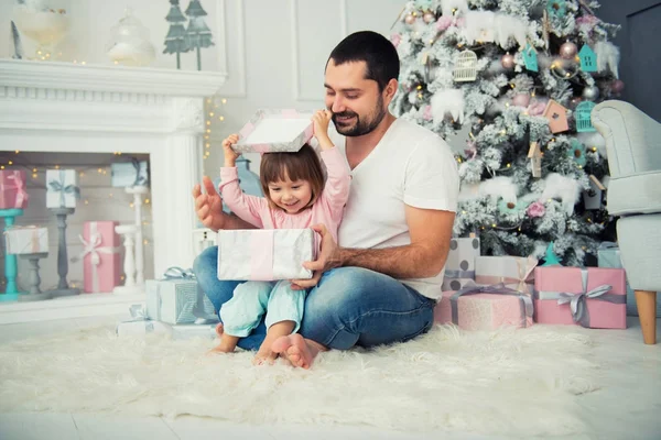 Tata i córka są siedzi i otworzenie świąteczny prezent w pobliżu choinki. Szczęśliwego nowego roku — Zdjęcie stockowe