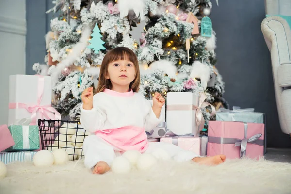 Emotional smiling little girl sitting in pajama with Christmas gifts near New Years tree and playing snowballs — Stock Photo, Image