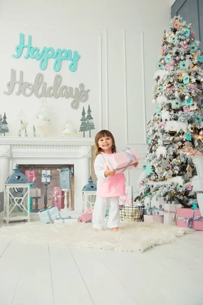Une heureuse petite fille souriante est debout avec des cadeaux de Noël près de l'arbre du Nouvel An. Vacances et cadeaux 2018 — Photo
