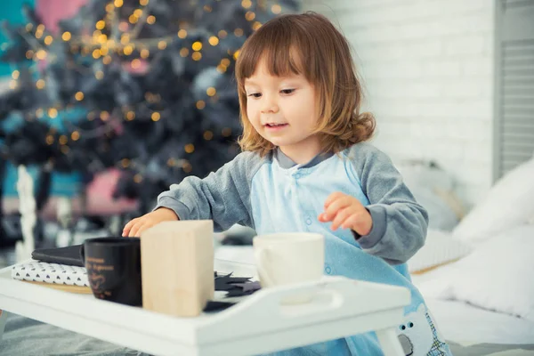 Emocional niña sonriente sentada en pijama con regalos de Navidad cerca del árbol de Año Nuevo y jugando bolas de nieve —  Fotos de Stock