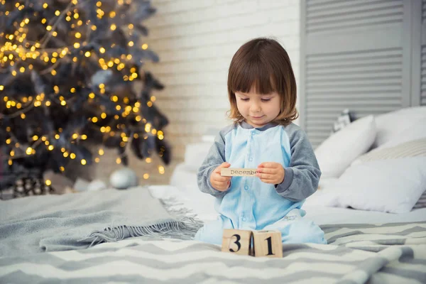 Emotional smiling little girl sitting in pajama with Christmas gifts near New Years tree and playing snowballs — Stock Photo, Image