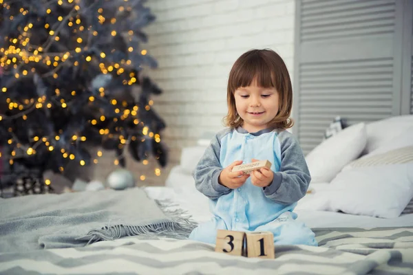 Емоційна усміхнена маленька дівчинка сидить у піжамі з різдвяними подарунками біля новорічної ялинки і грає в сніжки — стокове фото