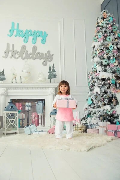 Une heureuse petite fille souriante est debout avec des cadeaux de Noël près de l'arbre du Nouvel An. Vacances et cadeaux 2018 — Photo