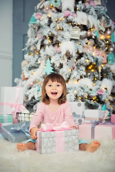 Positieve vrolijke babymeisje zit met de gift van Kerstmis in de buurt van de kerstboom. Gelukkig Nieuwjaar — Stockfoto