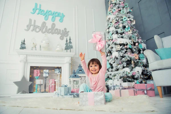 Positieve vrolijke babymeisje zit met de gift van Kerstmis in de buurt van de kerstboom. Gelukkig Nieuwjaar — Stockfoto