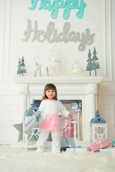 Щасливі маленька дівчинка усміхнений стоячи з різдвяні подарунки біля новорічної ялинки. Свята та подарунки 2018 — стокове фото