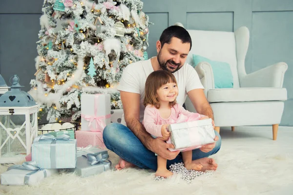 Tata i córka są siedzi i otworzenie świąteczny prezent w pobliżu choinki. Szczęśliwego nowego roku — Zdjęcie stockowe