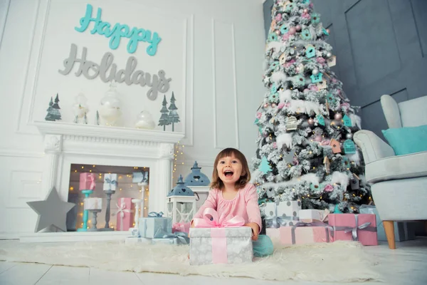 Pequena menina abre presente de Ano Novo perto da árvore de Natal — Fotografia de Stock