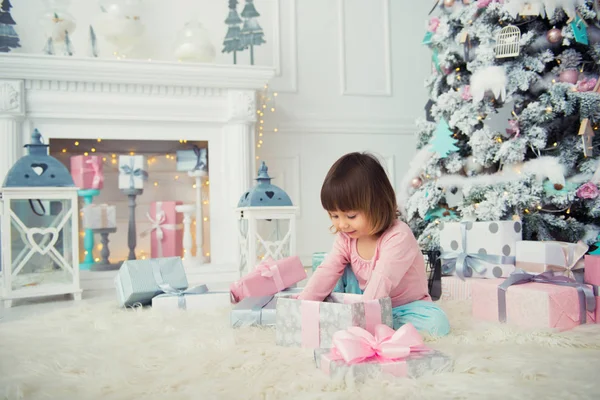 Positive fröhliche Baby-Mädchen sitzt mit Weihnachtsgeschenk in der Nähe von Weihnachtsbaum. frohes neues Jahr — Stockfoto