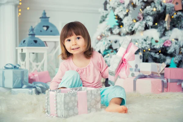 Pequena menina abre presente de Ano Novo perto da árvore de Natal — Fotografia de Stock